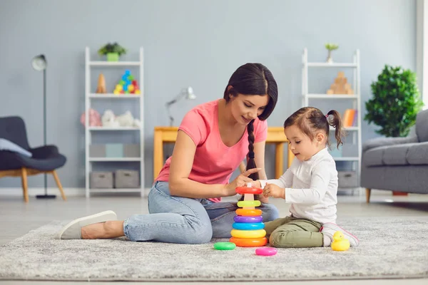 Spaanse moeder en dochter spelen met speelgoed terwijl ze op de vloer zitten in de kamer. — Stockfoto