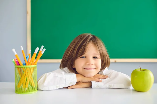 Torniamo a scuola. Divertente scolaro sorride mentre si siede alla paglia con libri in classe. — Foto Stock