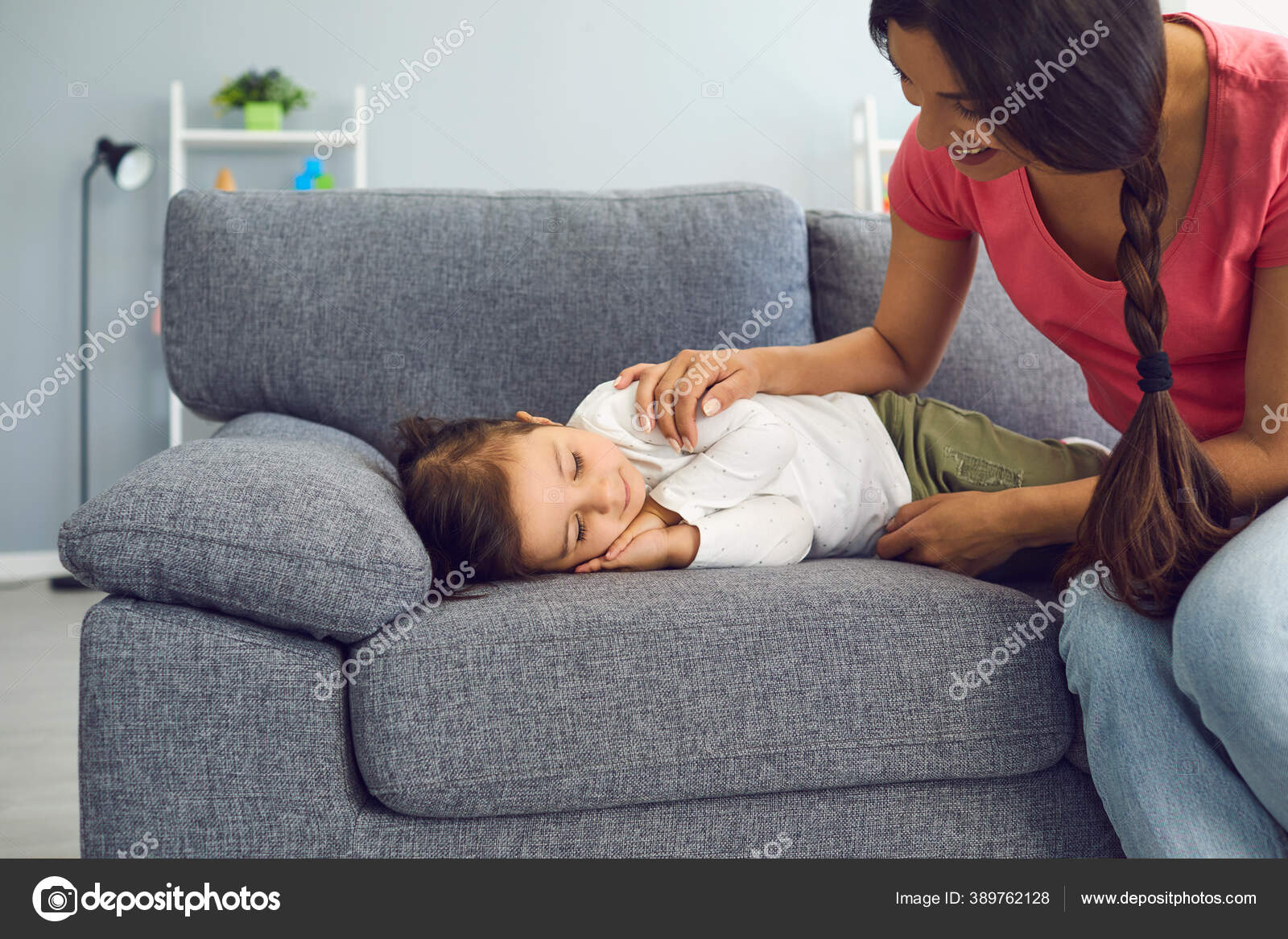 Jovem mãe feliz assistindo sua filha dormir no sofá na sala de estar. Pais  admirando seu filho cochilando em casa fotos, imagens de © lacheev  #389762128
