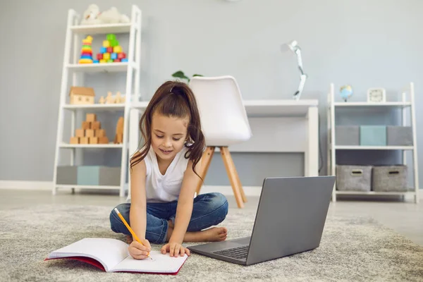 Educación en línea de los niños. Una niña pequeña hace una lección de profesor de una videolección una conferencia web de aprendizaje a distancia en casa . — Foto de Stock