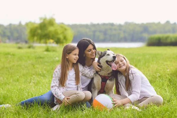 Anne kız ve köpek yakın planda çimenlerde oturuyor. Hafta sonları mutlu bir şekilde gülümsüyor.. — Stok fotoğraf