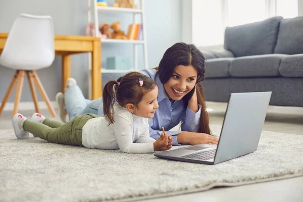 Lycklig mor och hennes söta lilla dotter tittar på online underhållning video tillsammans på laptop hemma — Stockfoto