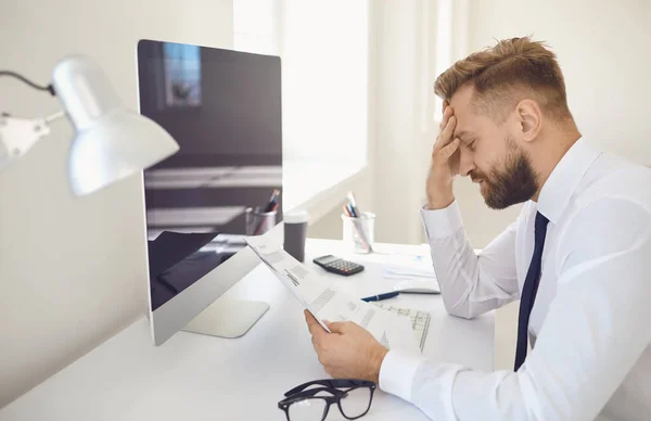 Allvarligt upptagen affärsman tror arbetsdokument sitter vid ett bord med en dator på kontoret. — Stockfoto