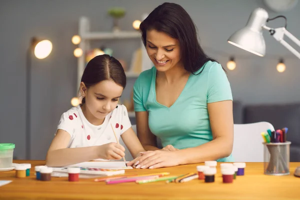 Moeder en dochter schilderen samen met verf en potloden. Familie activiteit en creativiteit idee. — Stockfoto