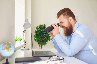 Dürbünü arayan komik bir adam. Ofiste çalışan bir dizüstü bilgisayar..