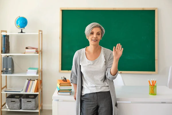 Le professeur dans la salle de classe. Femme avec professeur de cheveux gris a salué sa main tout en se tenant contre la classe. — Photo