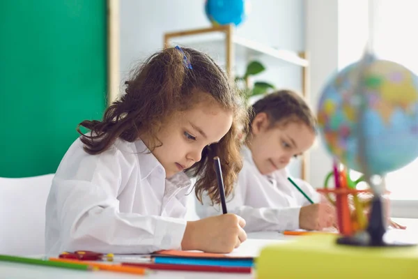 De vuelta a la escuela. Niños escolares escriben mientras están sentados a la mesa en el aula . — Foto de Stock