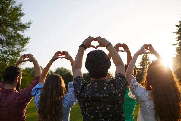 Handtekenhart. Een groep mensen houdt hand in hand met een hart teken op een hemel achtergrond met zonsondergang op de natuur. — Stockfoto