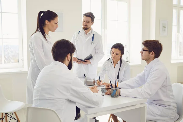 Grupo de médicos praticantes em uma reunião discutir o diagnóstico de um paciente de pé em um consultório de clínica . — Fotografia de Stock