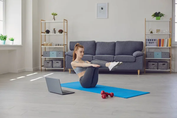Fitness girl robi ćwiczenia na podłodze i oglądanie filmu treningowego podczas posiadania laptopa w salonie. Filmik treningowy online w domu. — Zdjęcie stockowe