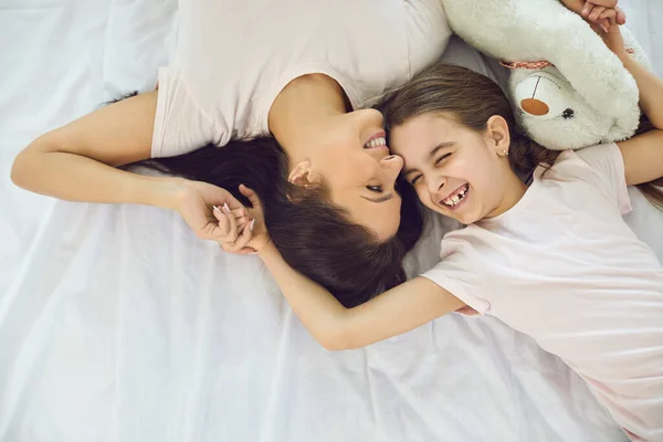 Вид зверху на дівчину, яка сміється з матір'ю в ліжку. Чарівна дитина і любляча мама розслабляється перед сном — стокове фото