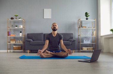 Çevrimiçi yoga dersi. Huzurlu genç adam evde dizüstü bilgisayarın önünde meditasyon yapıyor. Yaşam dengesi kavramı