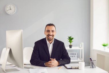 Masada oturan siyah ceketli esmer bir adam ofiste kağıtlarla çalışıyor..