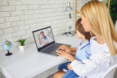 Çevrimiçi doktor. Çocuğu olan hasta anne, oturma odasındaki masada oturan bir doktor terapistine video görüşmesi yapıyor..