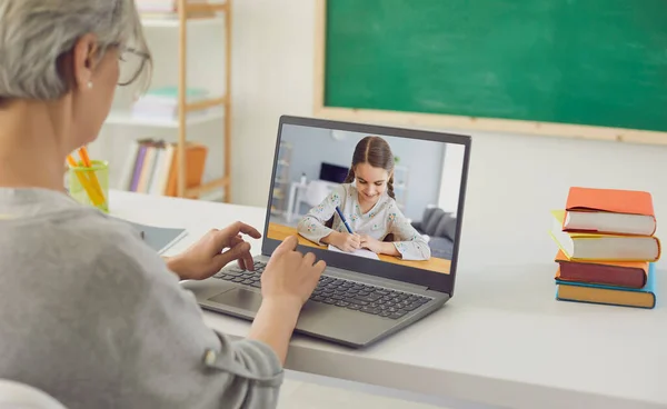 Insegnante online insegna a un bambino. La bambina scrive una lezione in un quaderno usando una videochat con un insegnante di laptop a casa da remoto. — Foto Stock