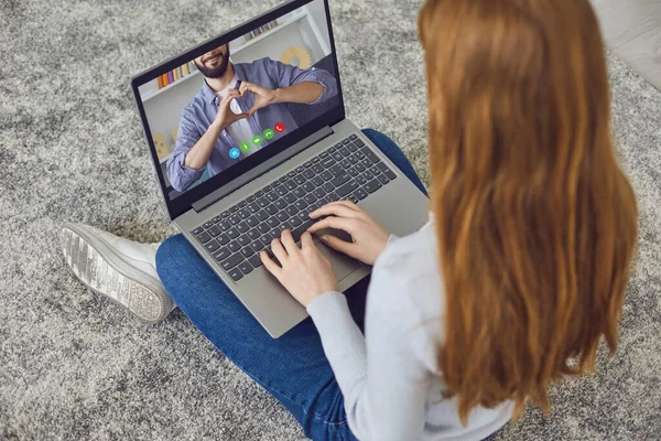 Date Dating online. Herzzeichen mit männlichen Händen im Laptop-Monitor eines jungen Mädchens, das zu Hause auf dem Boden sitzt. — Stockfoto