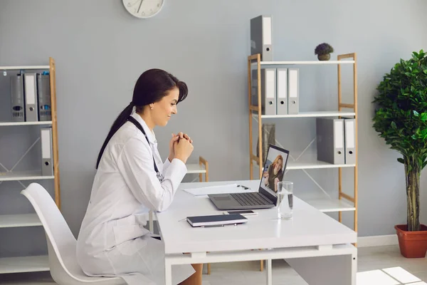 Kobieta lekarz słucha pacjenta za pomocą kamery wideo laptopa w gabinecie kliniki. — Zdjęcie stockowe