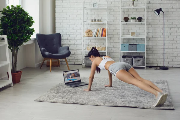 Entrenador de entrenamiento online. Chica atlética en ropa deportiva gris está haciendo ejercicios tiene un entrenamiento de vídeo portátil en casa — Foto de Stock