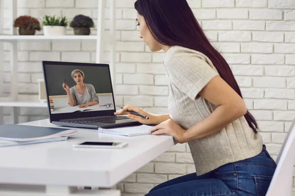 Online oktató tanár. A fejhallgatós lánynak van egy web call lecke laptopja otthon egy asztalnál.. — Stock Fotó