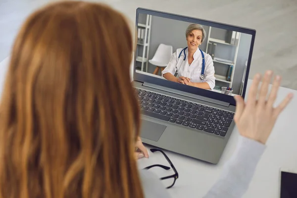 Online orvos. Idősebb nő orvos ősz hajjal hallgat beteg video chat számítógép otthon. — Stock Fotó