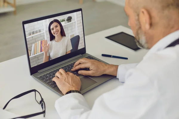 Médico e paciente online. Paciente menina diz que consulta usando webcam laptop com médico homem sênior na clínica virtual . — Fotografia de Stock