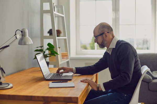 Arbeiten Sie online. Älterer Mann tippt Laptop-Text ein, während er zu Hause an einem Tisch sitzt. — Stockfoto