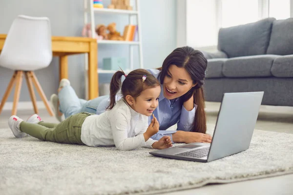 Lycklig mor och hennes söta lilla dotter tittar på online underhållning video tillsammans på laptop hemma — Stockfoto