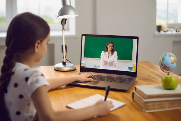 Zdalne kształcenie dzieci. Dziewczynka ogląda lekcję wideo z laptopa kursu nauczycielskiego siedzącego przy stole w salonie. — Zdjęcie stockowe