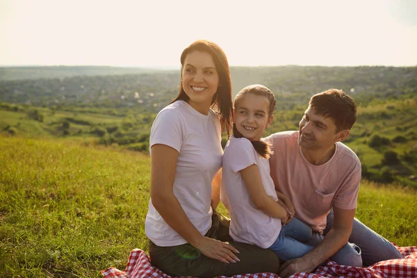 Vahşi doğada piknik battaniyesinde oturan kızı olan bin yıllık ebeveynler. Çocuklu bir aile, yaz gününün tadını çıkarıyor. — Stok fotoğraf