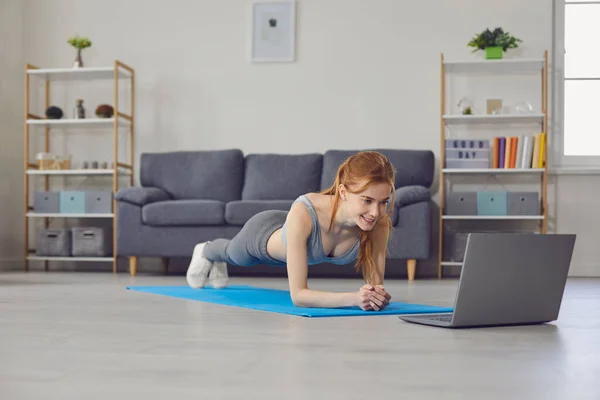 온라인 홈 스포츠. 예쁜 아가씨 가 거실에서 랩탑 컴퓨터를 가지고 놀고 있어. 팔꿈치로 농구공을 하는 여자 — 스톡 사진