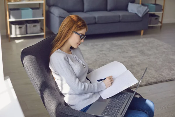 Online-Heimtraining. Das Mädchen macht die Lektion eines ferngesteuerten Laptop-Lehrers, der auf einem Stuhl im Zimmer sitzt. — Stockfoto