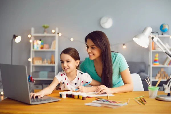 Онлайн-обучение для детей. Мать и дочь смотрят видео урок рисования лекции с помощью компьютера в гостиной . — стоковое фото