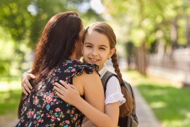 Sırt çantalı sevimli kız okula giderken annesine sarılıyor. Okula geri dön..