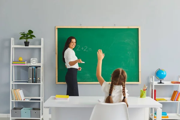 Повернутися до школи. Маленька дівчинка піднімає руку, щоб відповісти на її вчителя на уроці математики . — стокове фото