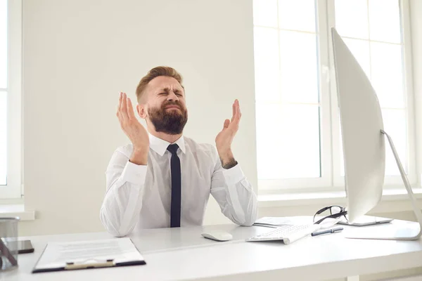 Расстроенный уставший бизнесмен поднял руки, глядя на компьютер за столом в офисе . — стоковое фото