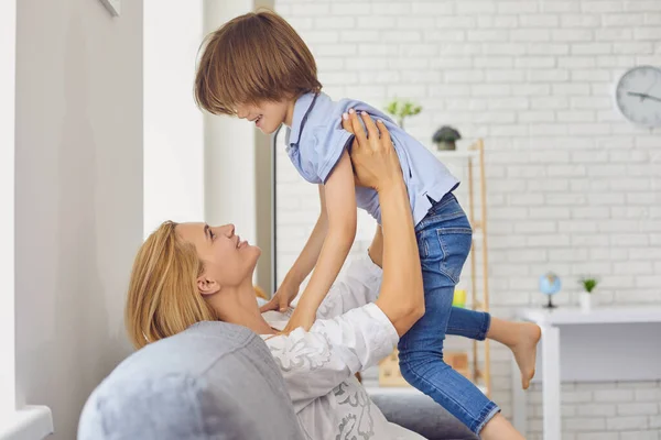 Ibu yang bahagia mengangkat anaknya ke udara di rumah. Orangtua bermain game dengan anak kecil, bersenang-senang di ruang tamu — Stok Foto