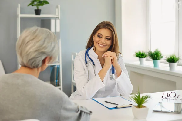 Freundliche junge Ärztin, die einen älteren Patienten in der Klinik berät. Reife Frau zu Besuch beim Facharzt im Krankenhaus — Stockfoto