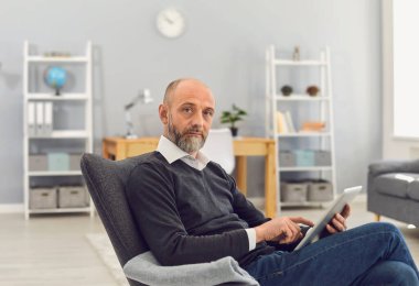 Tablet bilgisayarı olan olgun bir adam internette çalışıyor, ailesiyle sohbet ediyor, doktora danışıyor ya da evde Webinar izliyor.