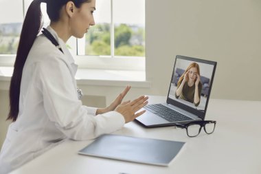 Online doktor ve hasta. Başı ağrıyan hasta bir kız bilgisayar kamerası kullanarak doktora video araması yapıyor..