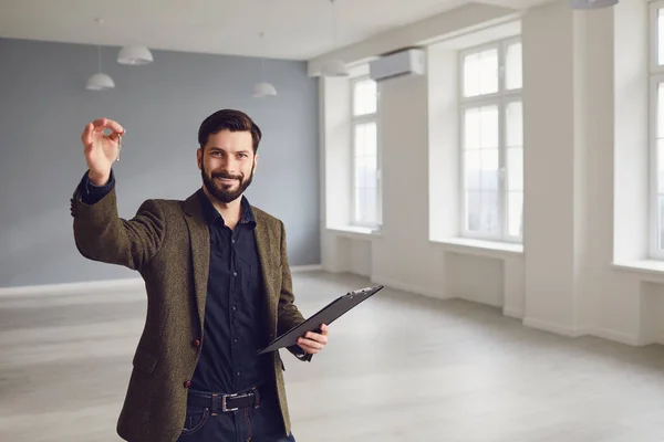 Agente de bienes raíces es un agente inmobiliario con las llaves en la mano en el fondo de una casa de la habitación de bienes raíces blanca . — Foto de Stock