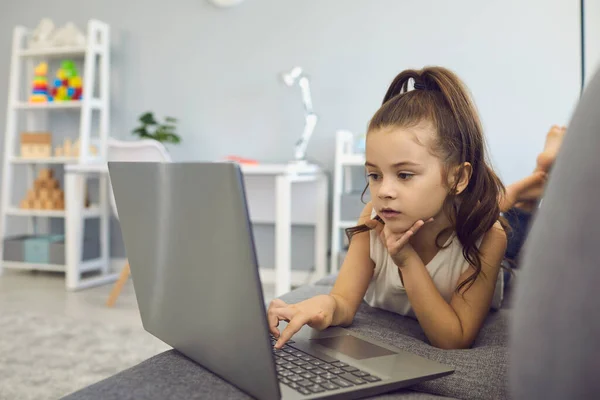 Дистанційне навчання. Маленька дівчинка використовує ноутбук для онлайн-класу вдома. Мила дитина дивиться освітнє відео в Інтернеті — стокове фото