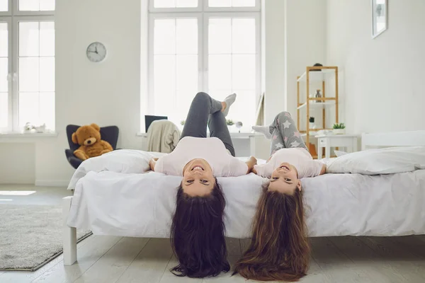 Mãe alegre e filha com cabelo bonito deitado de cabeça para baixo na cama em casa. Pais e criança se divertindo no quarto — Fotografia de Stock