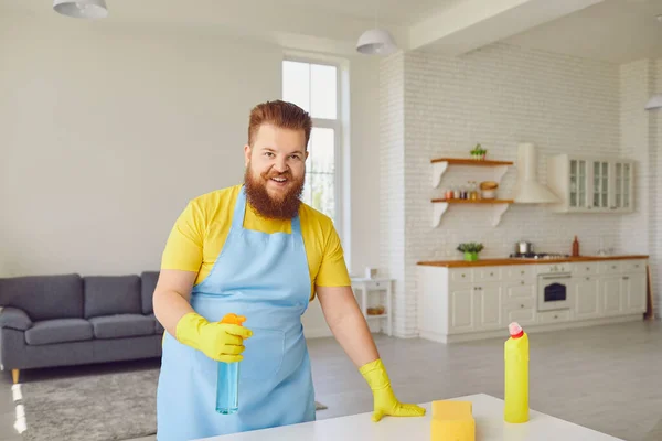 Hombre gordo divertido con barba en un delantal limpia la habitación de la casa . — Foto de Stock