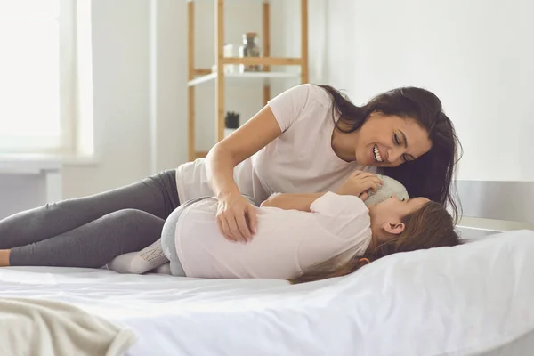 Glückliche Mutter umarmt ihre Tochter zu Hause im Bett. Liebevolle Mutti mit Kind lacht zusammen und entspannt sich morgens — Stockfoto