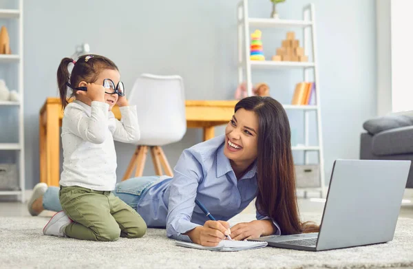 Annesi evde online serbest iş yaparken sevimli bir kız gözlüklerle oynuyor. Evden çalışmak ve ebeveynlik — Stok fotoğraf