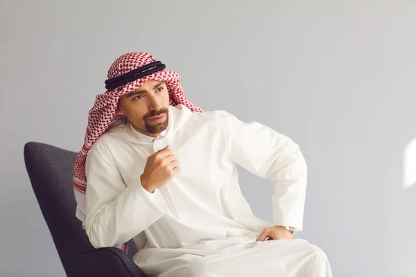 Страшный арабский бизнесмен, сидящий в кресле, думает, что смотрит на серый фон. Портрет привлекательного араба. — стоковое фото