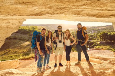 Dağlarda bir mağarada sırt çantalı turist grupları birlikte kameraya bakarlar..