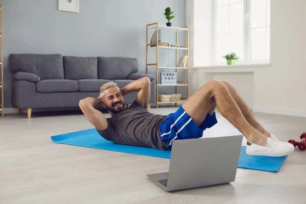 집에 있는 노트북에서 온라인 비디오 강의를 하고 있는 젊은이입니다. 실내에서 요가 매트 위에서 그림 운동을 하는 뚱뚱 한 남자 — 스톡 사진