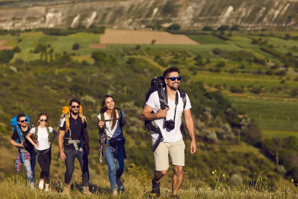A group of friends with backpacks on a hike in nature. Young people tourists are walking on a hill in the mountains.