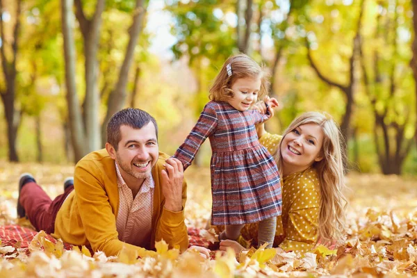 Family lying on yellow leaves in the park in autumn. — Stock Photo, Image